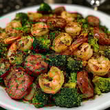 A plate of food with shrimp, sausage, and broccoli.