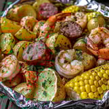 A bowl of food with shrimp, sausage, potatoes, corn and peppers.