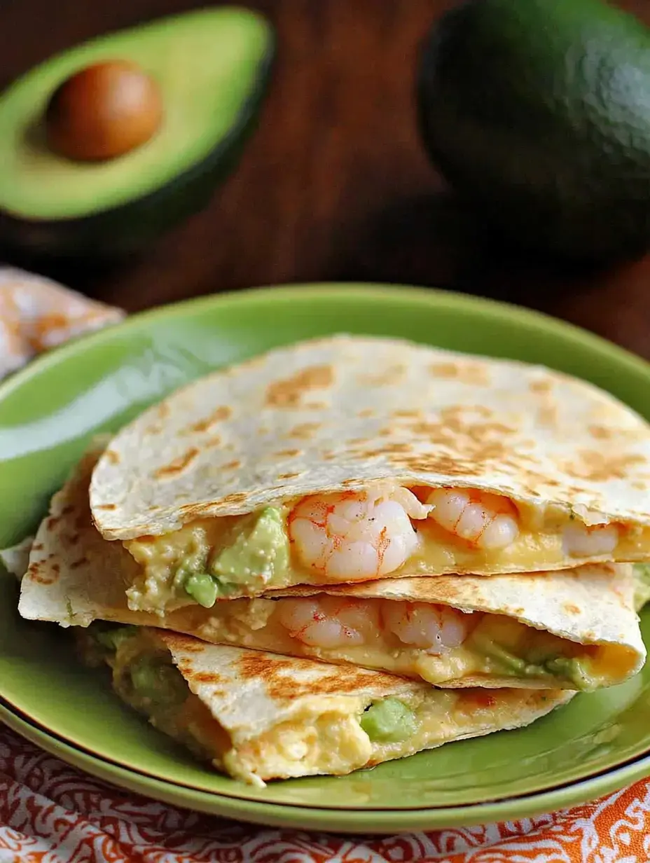 Shrimp and avocado quesadillas piled on a green plate with a cut avocado sitting in the background slightly out of focus.