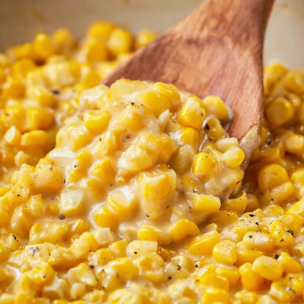 A wooden spoon in a bowl of corn.