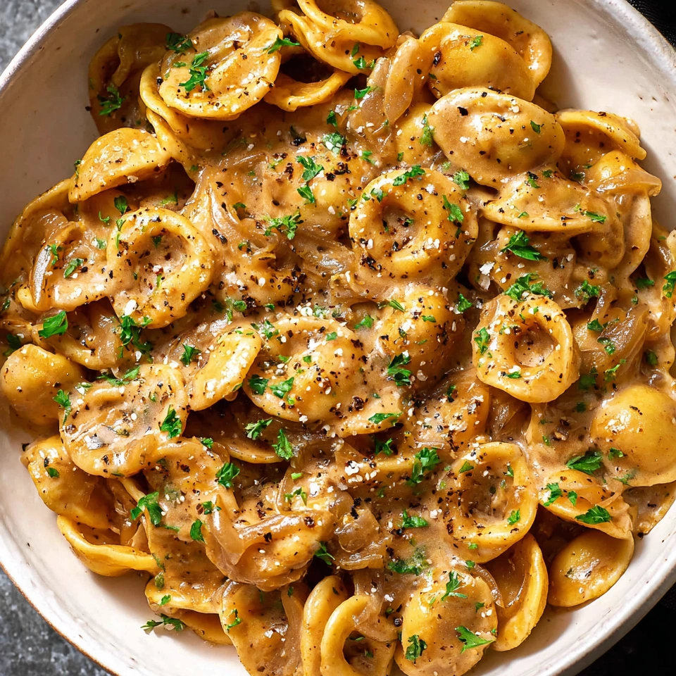 A bowl of pasta with a creamy sauce and onions.