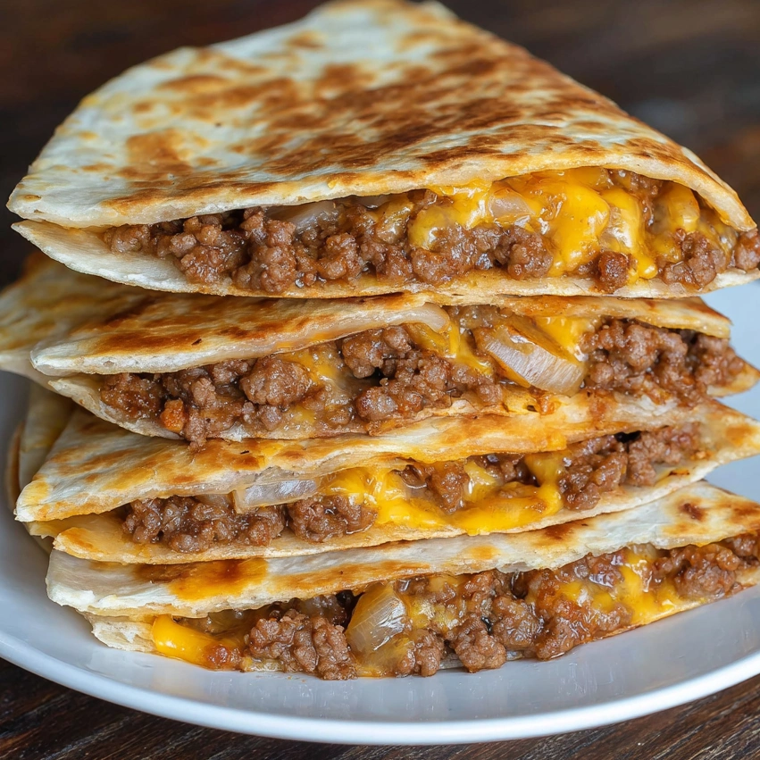 Bacon cheeseburger quesadillas stacked on a plate.