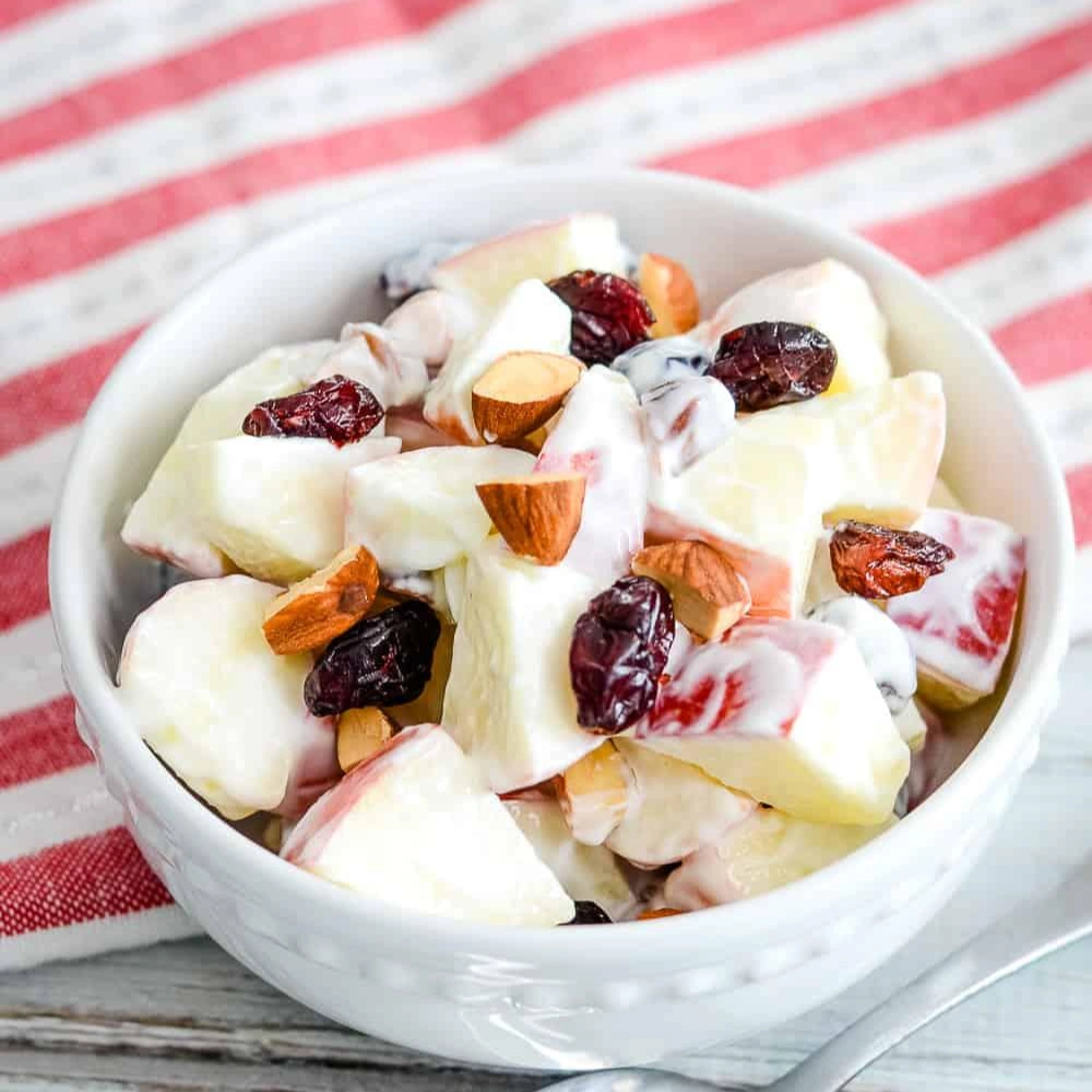 A bowl of fruit salad with apples, nuts, and raisins.
