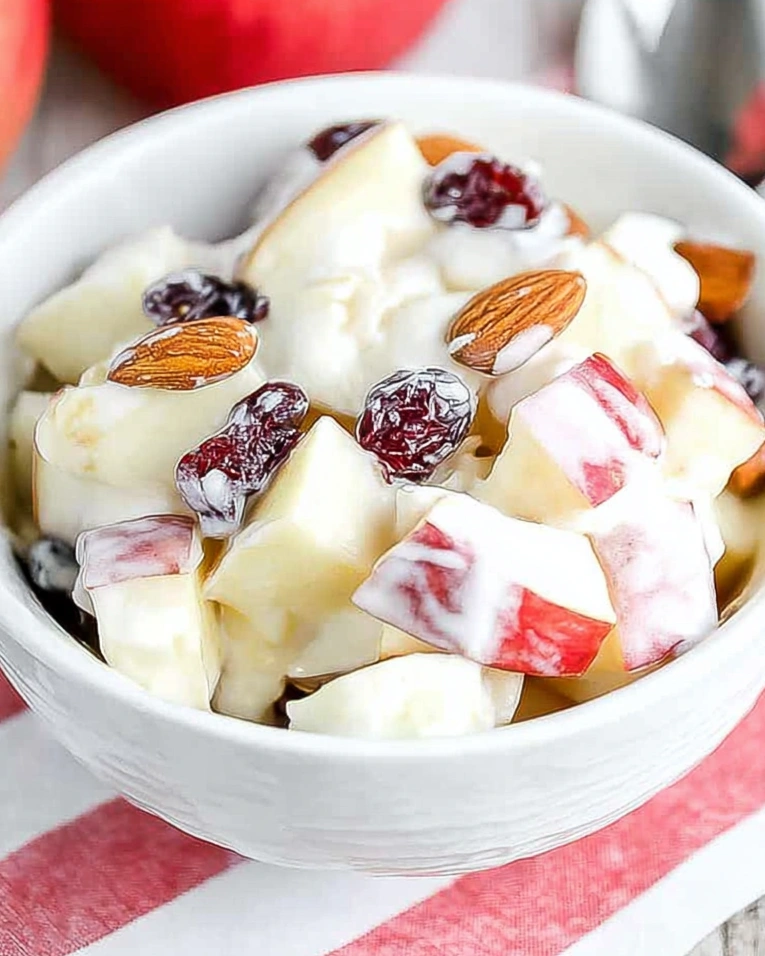 A bowl of fruit salad with apples and raisins.