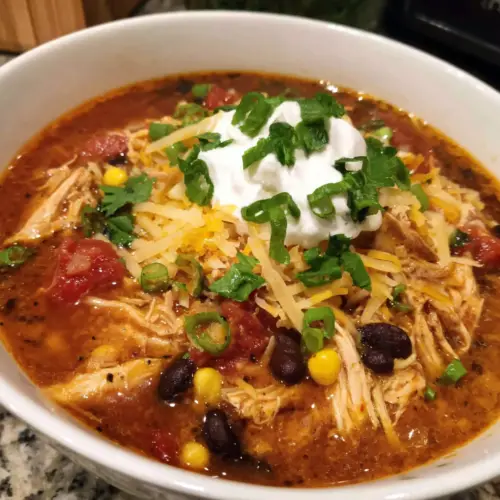 A bowl of chili with cheese and chicken.