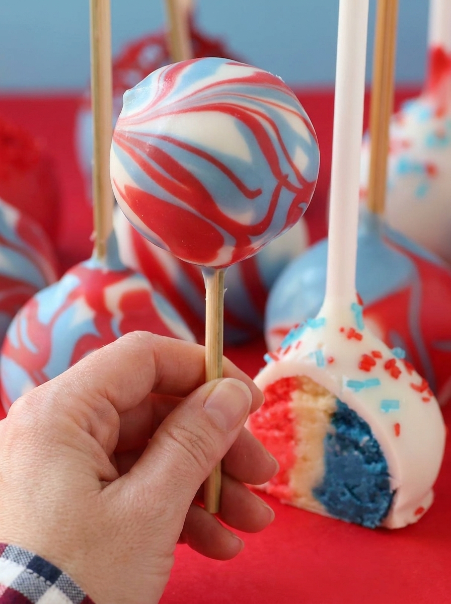 A hand holding a cake pop with red, white and blue colors.