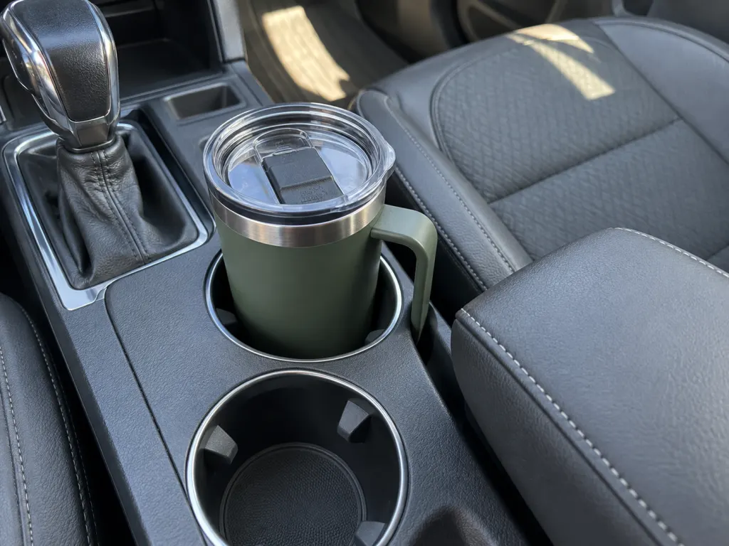 Handled travel mug sitting securely in a car cup holder beside the center gap.